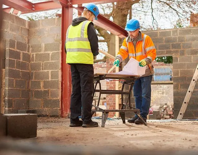 Builders reviewing structural drawings on site next to a steel frame